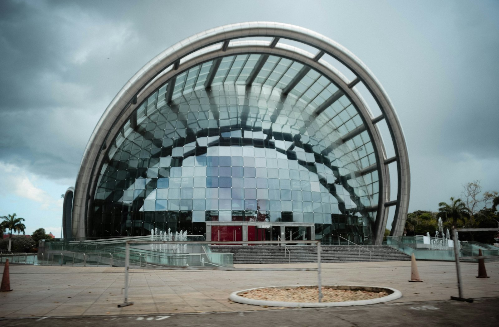 Glass and steel arch of the NAPA building on Frederick Street, Port of Spain, under a cloudy sky